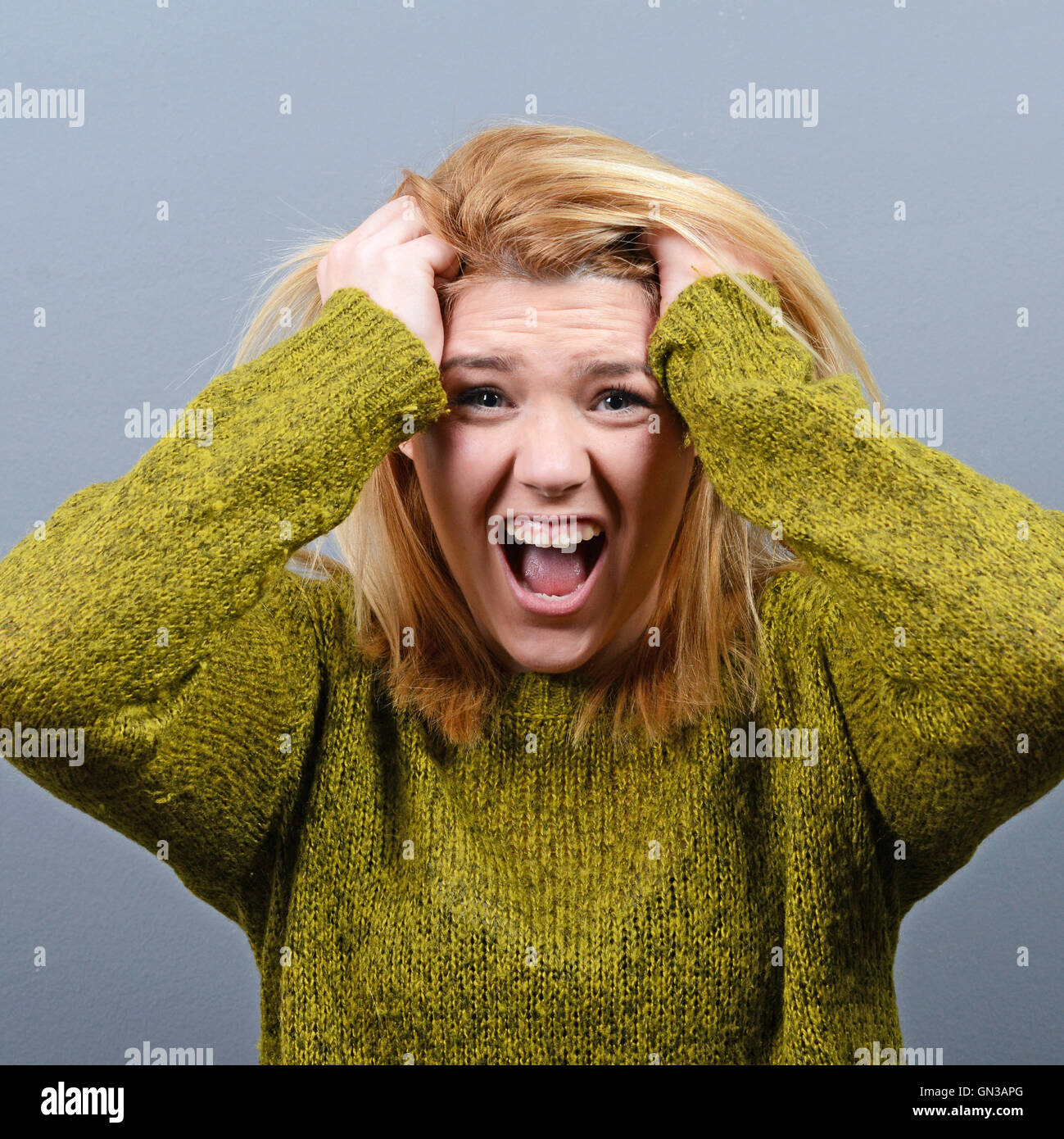 Portrait of a histerical woman pulling hair out against gray background