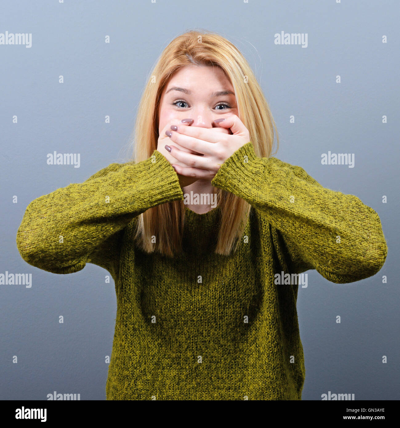 Woman covering her mouth with hands against gray background Stock Photo ...