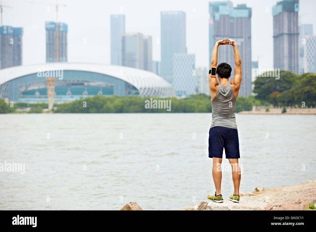 young asian male jogger with fitness tracker attached to arm warming up