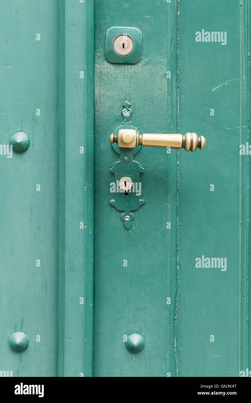 A green painted wooden door with a bronze door handle and two key holes. Stock Photo