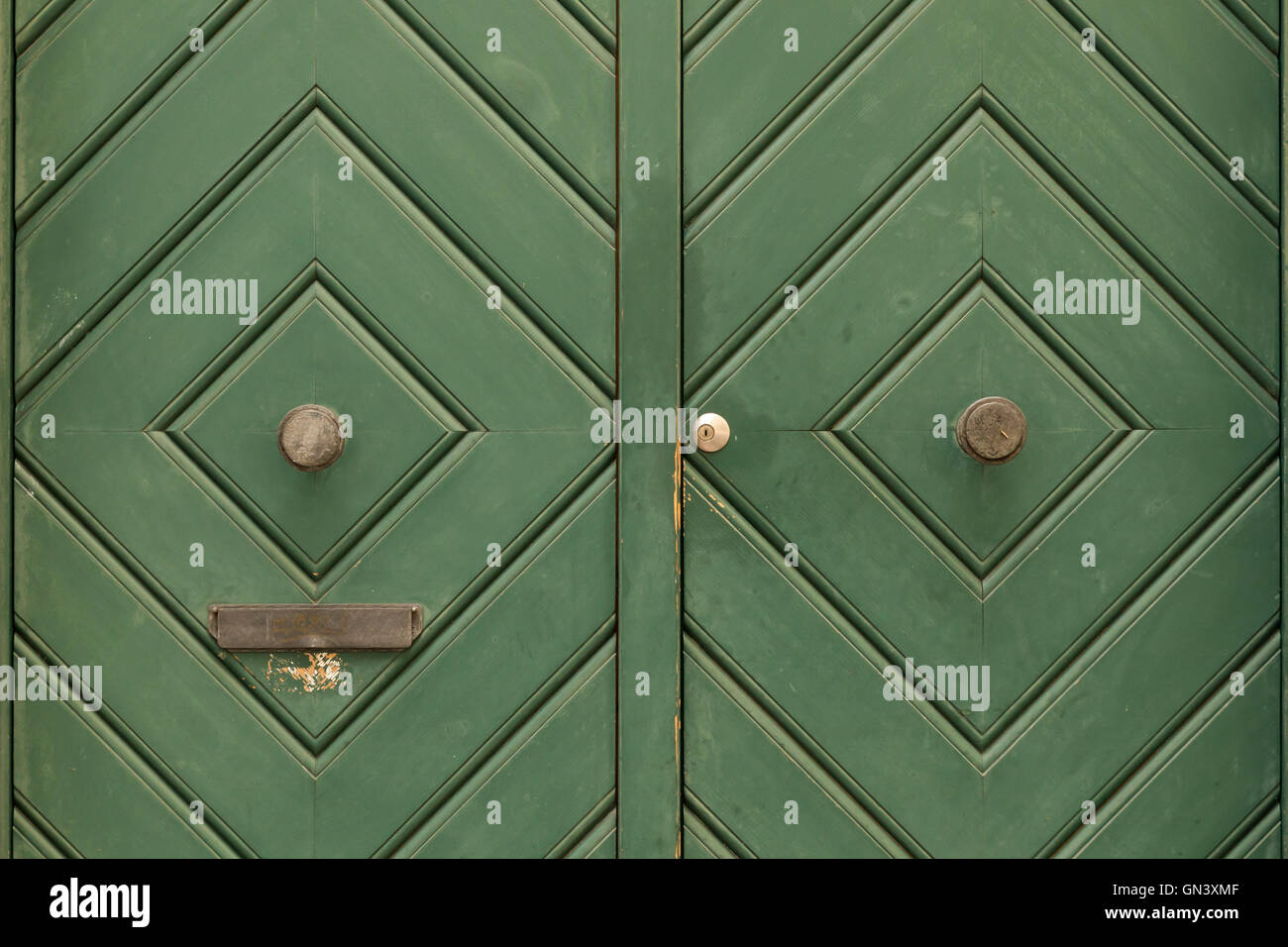 A green painted wooden double door with diamond pattern and round door knob. The left door side has a slit for mail. Stock Photo
