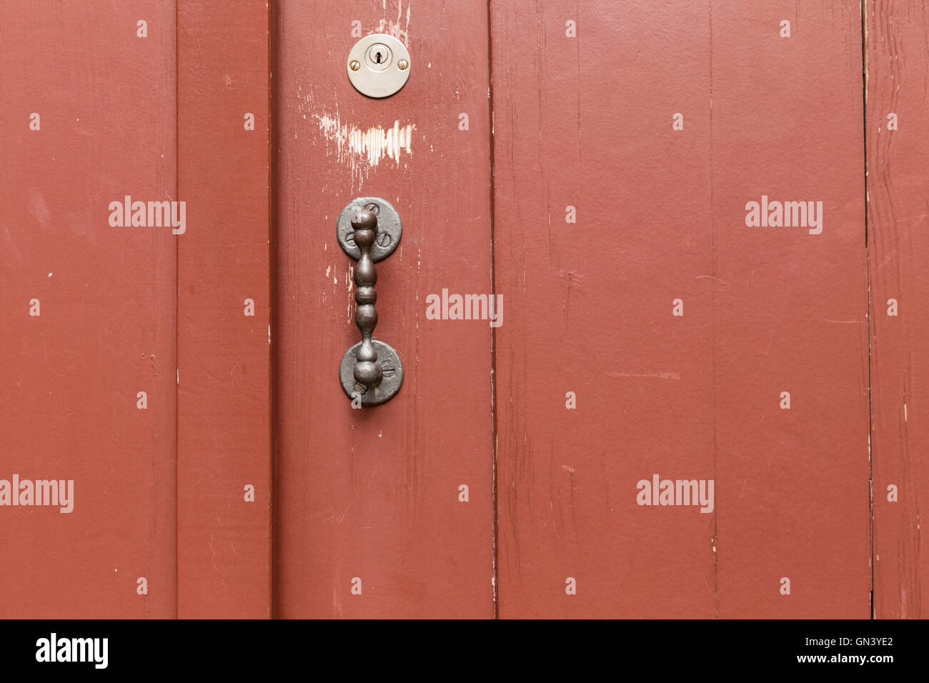 A red painted wooden door with vertical planks, metal door handle and