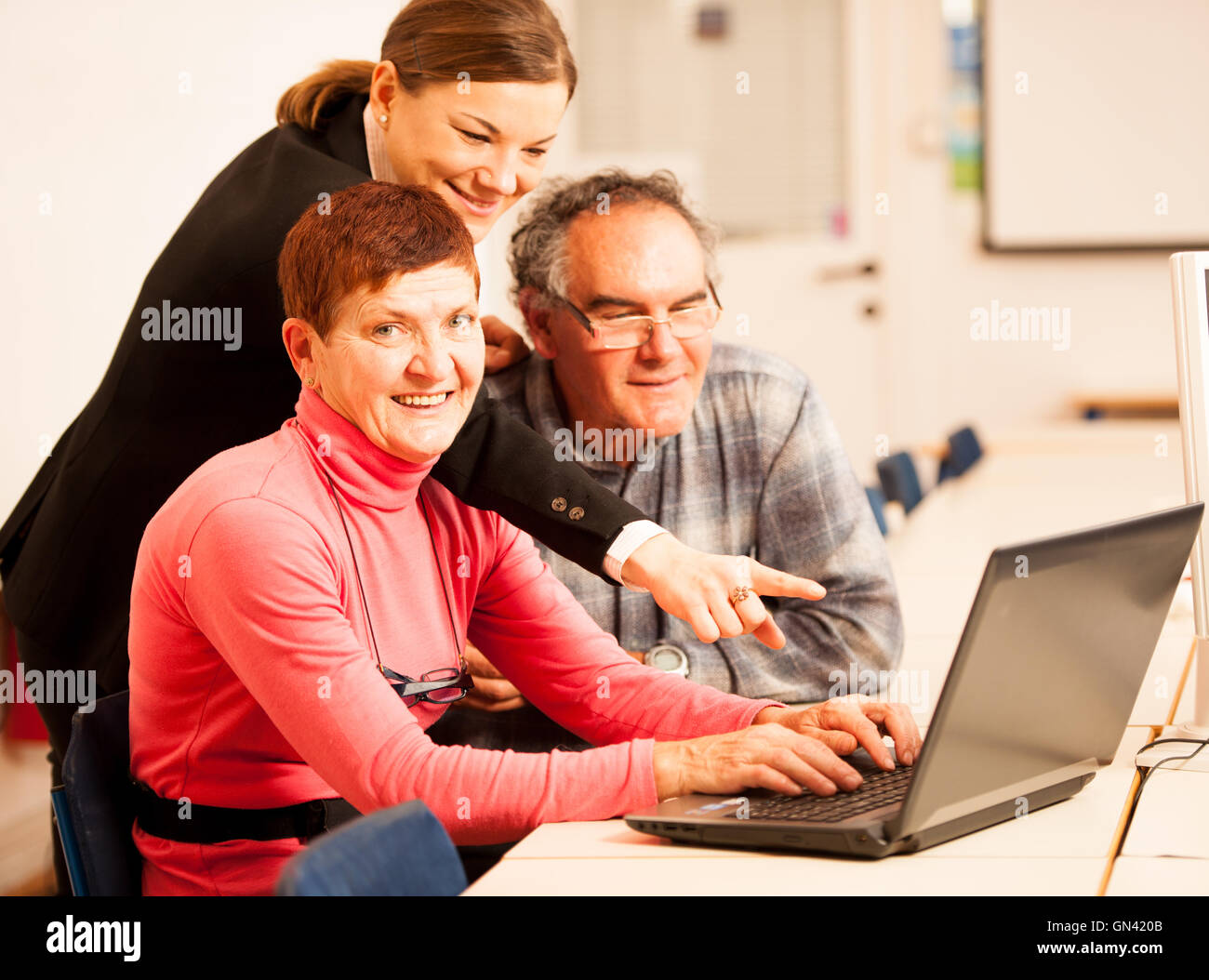 Young woman teaching elderly couple of computer skills. Intergenerational transfer of knowledge. Stock Photo