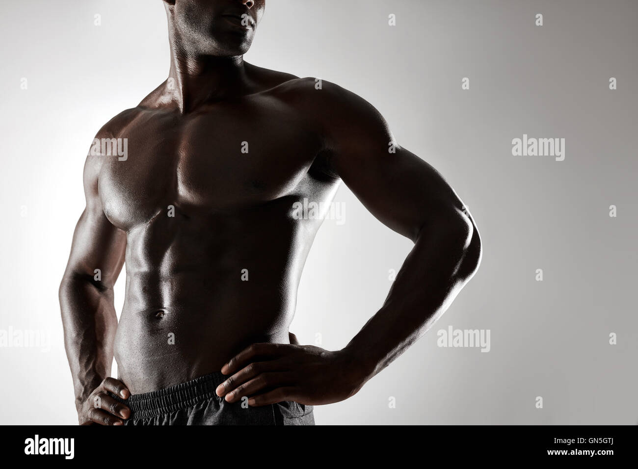 Cropped shot of young man with muscular body standing against grey background. Shirtless male model with hands on hips. Stock Photo