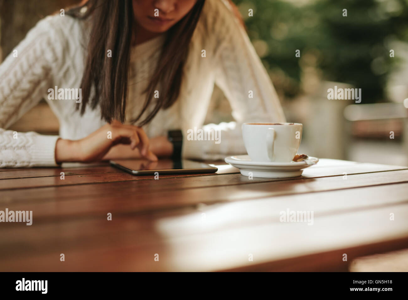 Cropped shot of woman using digital tablet while sitting at table with cup of coffee. Female surfing internet on touch screen co Stock Photo