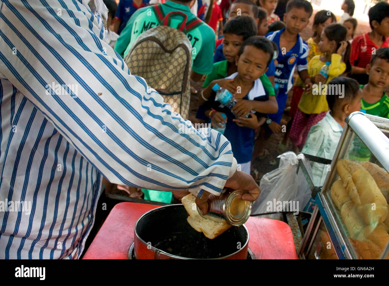 A vendor is pouring sweetened condensed beverage creamer on bread as a group of young Cambodian students await their snacks in Stock Photo