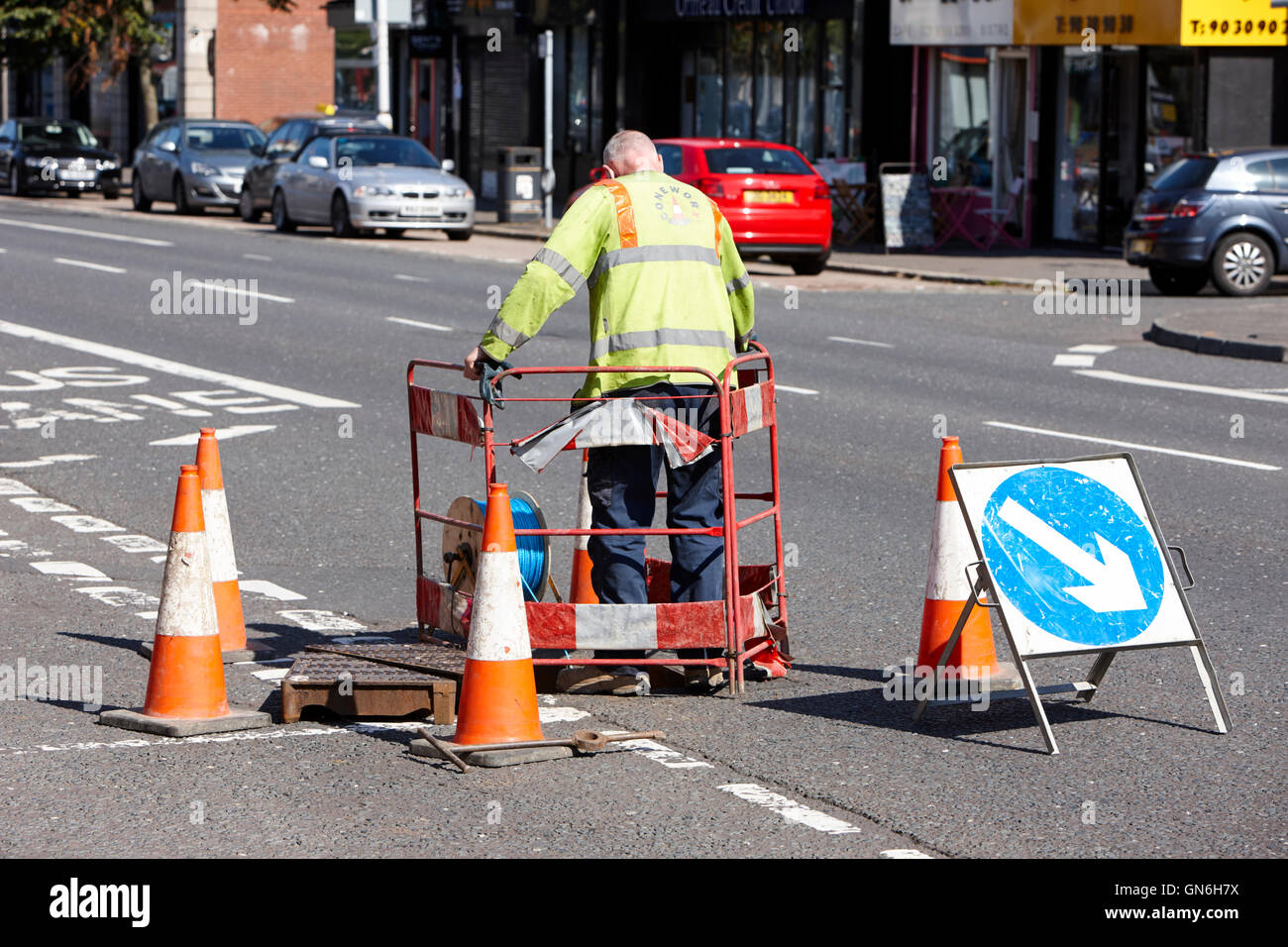 man sets up temporary traffic barrier on road to facilitate utility access to manhole Stock Photo