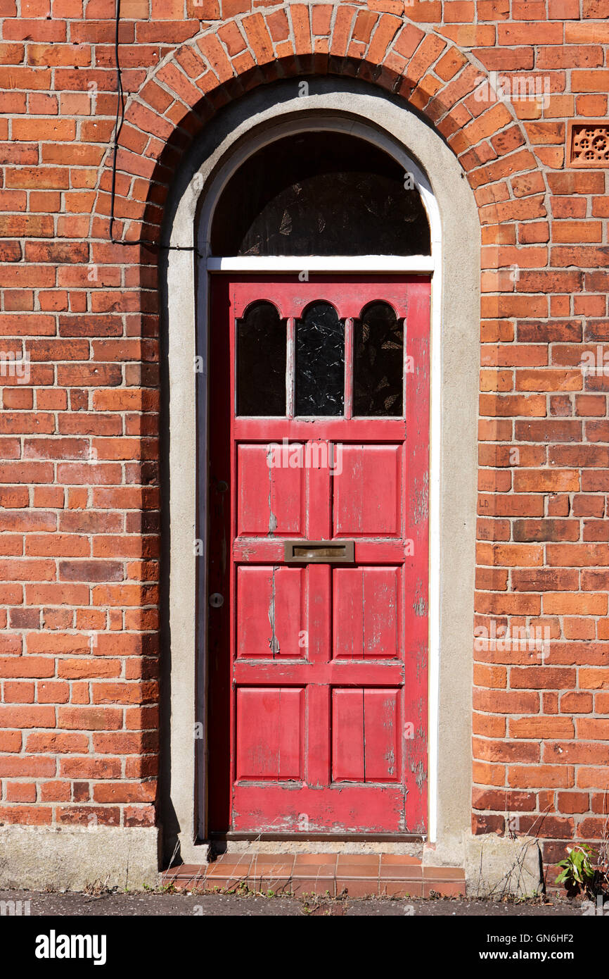 peeling red paintwork in a wooden door in an arched doorway of red brick victorian two up two down house in the uk Stock Photo