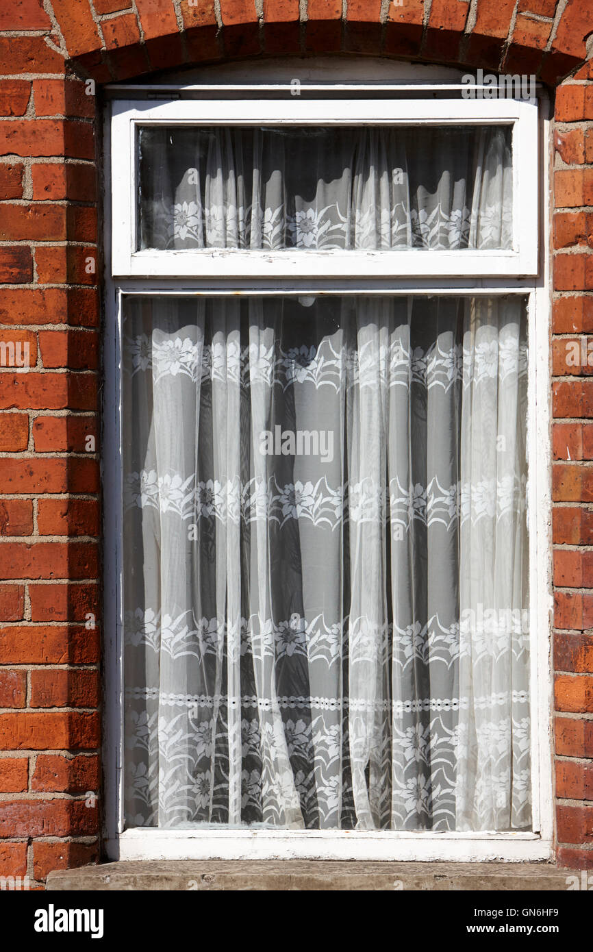 old net curtains hanging in the window of a red brick victorian terraced house Stock Photo