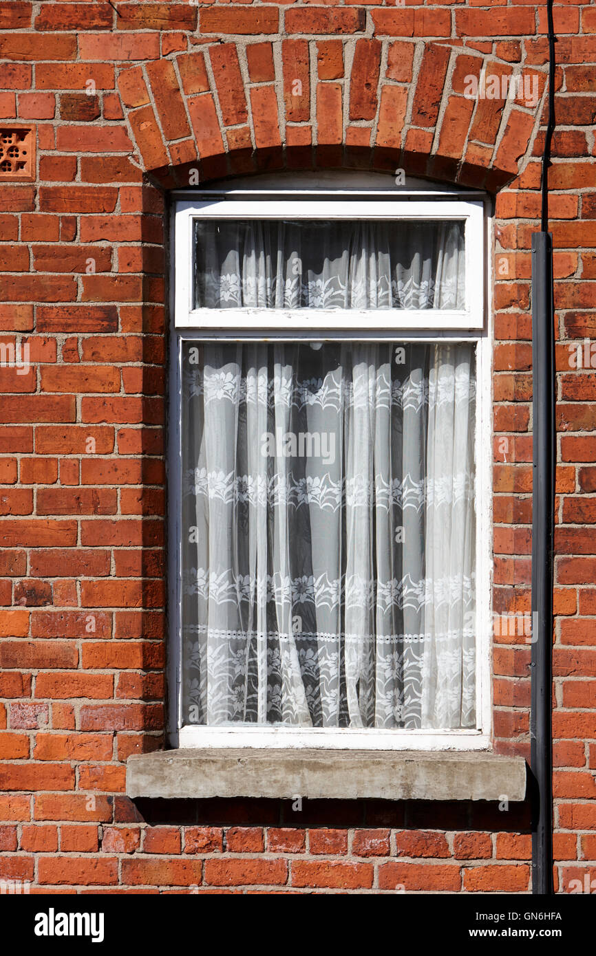 old net curtains hanging in the window of a red brick victorian terraced house Stock Photo