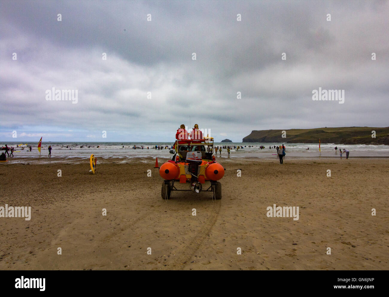 Two Female RNLI lifeguards keep watch as people learn to surf on a chilly summer morning at Polzeath Beach, North Cornwall, UK Stock Photo