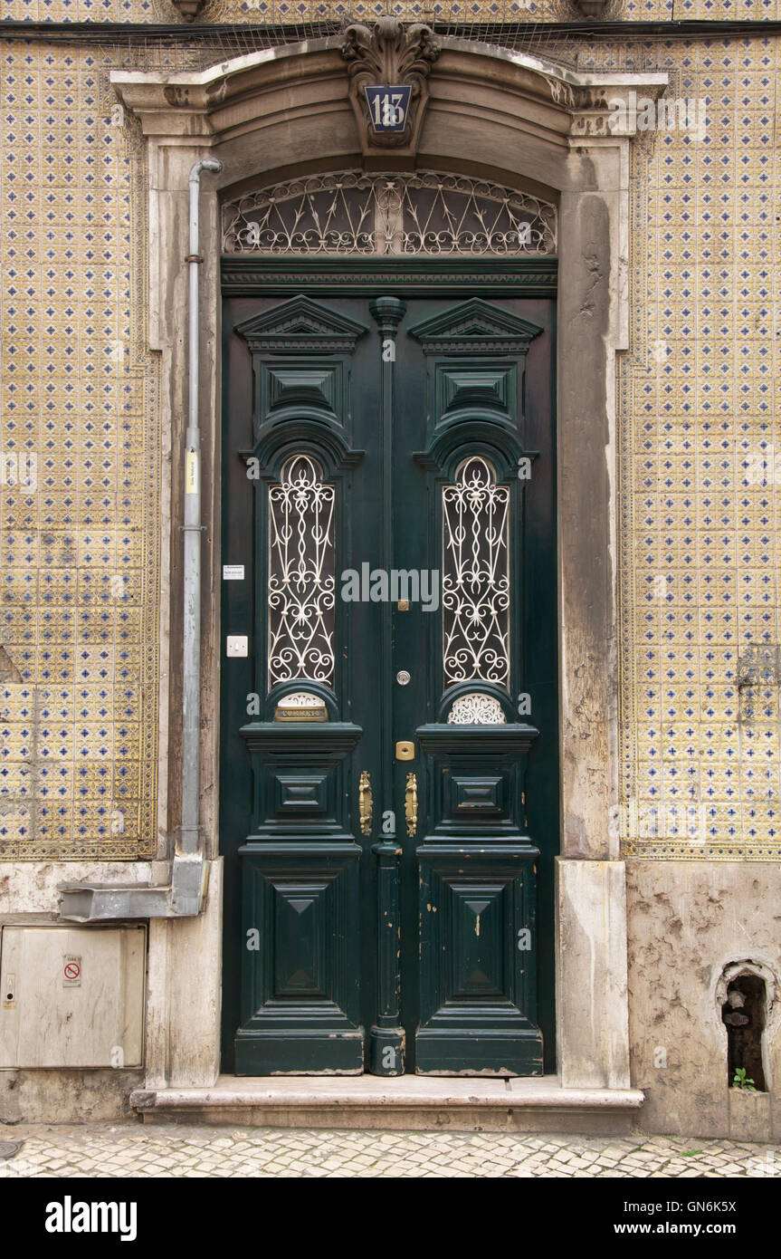 An old ornate green door in a city street, surrounded by traditional Portuguese ceramic wall tiles (azulejo). Lisbon, Portugal. Stock Photo