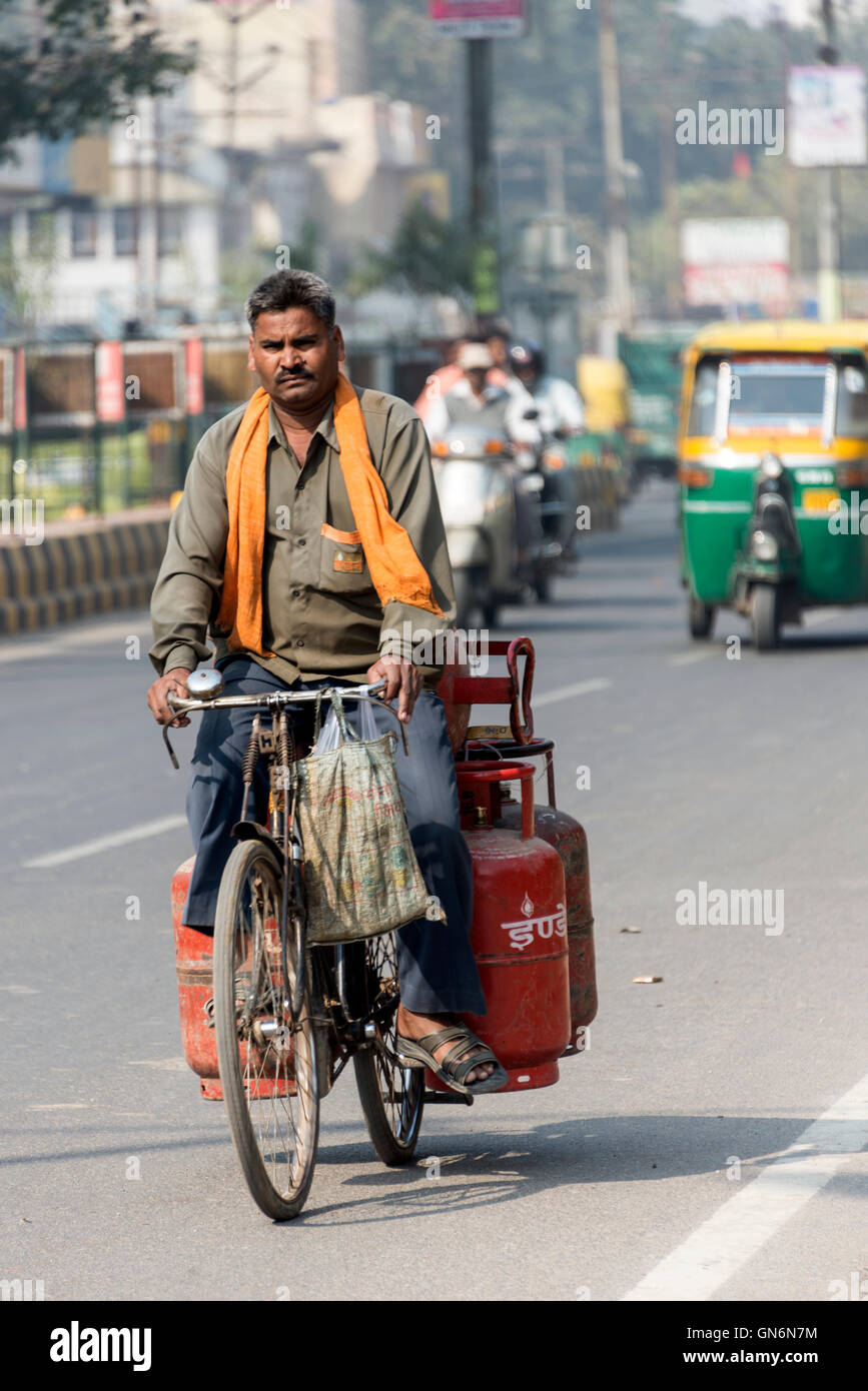 A cyclist riding his bike carrying full gas cylinders on a busy main road in Agra, Uttar Pradesh, India The tourist sign to the Stock Photo