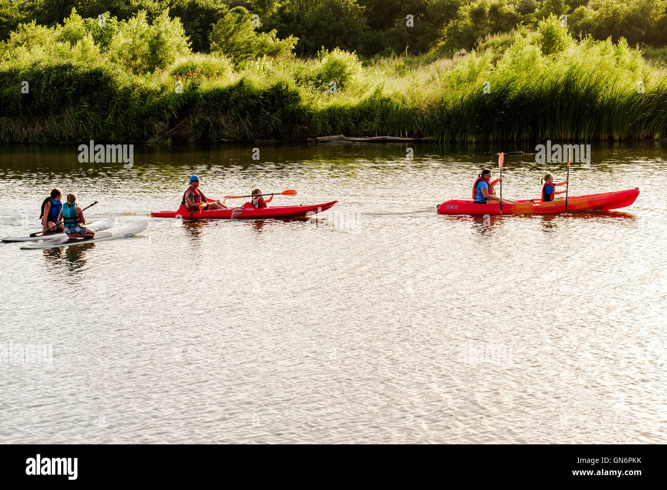 A father and mother each with a daughter in two canoes while two paddleboarders look on. Oklahoma, USA. Stock Photo