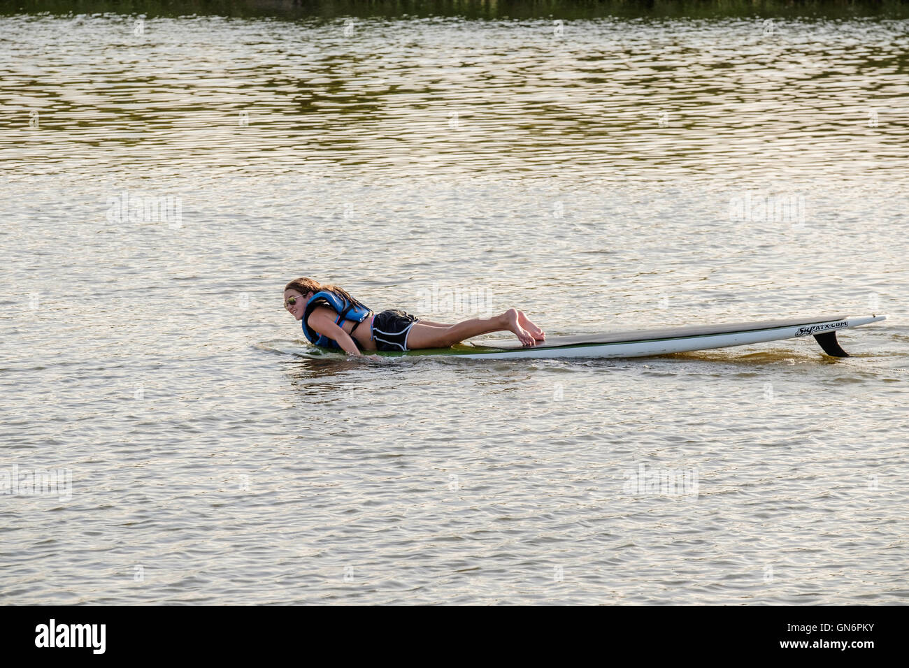 A 25-30 year old Caucasian woman paddles her paddle board with her arms after losing the paddle in a river. Oklahoma, USA. Stock Photo