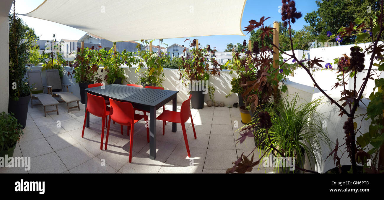 The terrace of a flat furnished with a set of garden furniture, deck chairs and a shade sail. Roof terrace. Flat upper terrace. Stock Photo