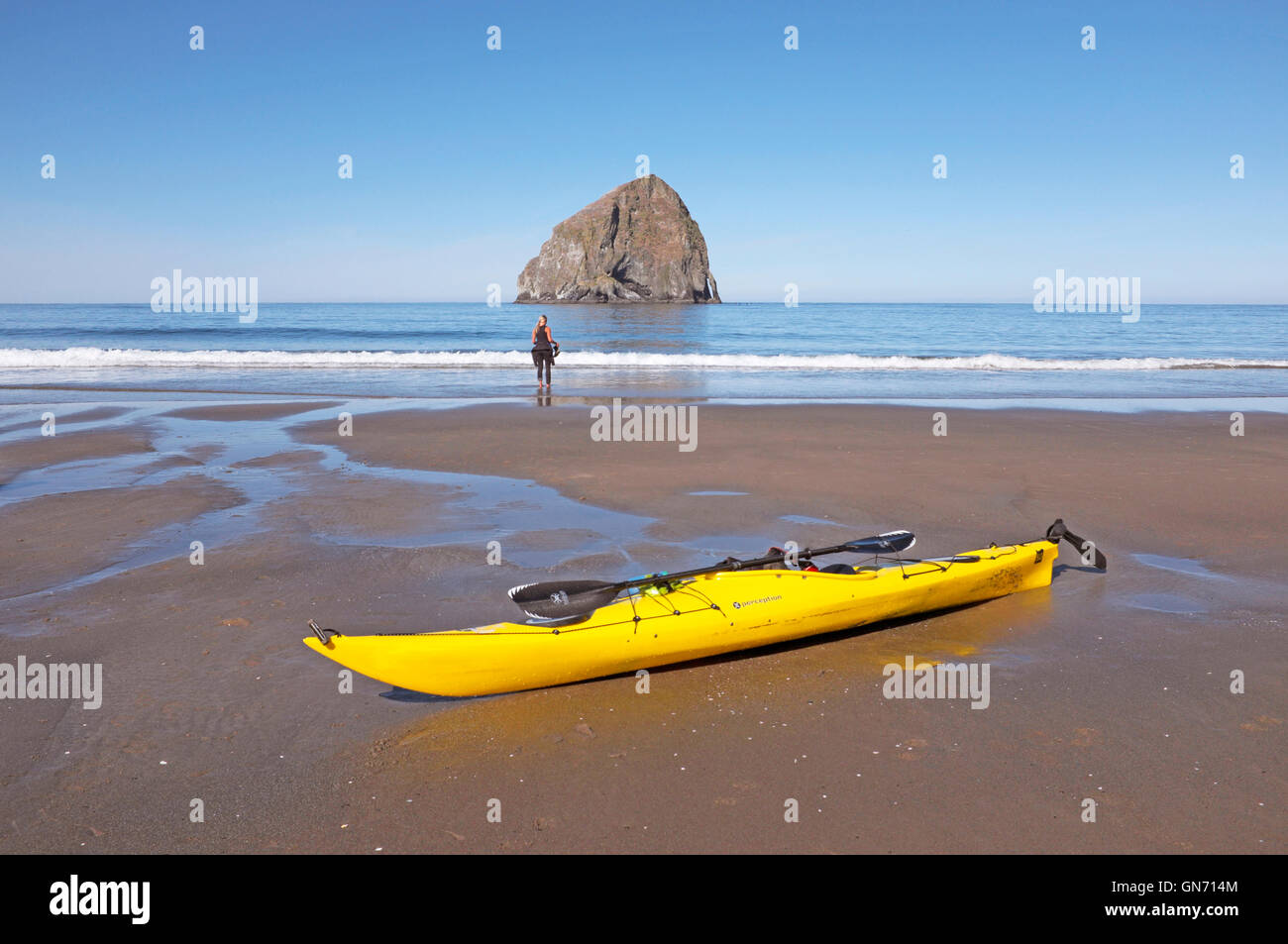 A sea kayak and kayaker on the beach in front of Haystack Rock, Pacific City, Oregon Stock Photo