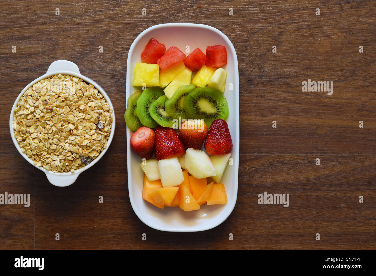 Bowl of granola and fruit platter on a wooden table. Healthy