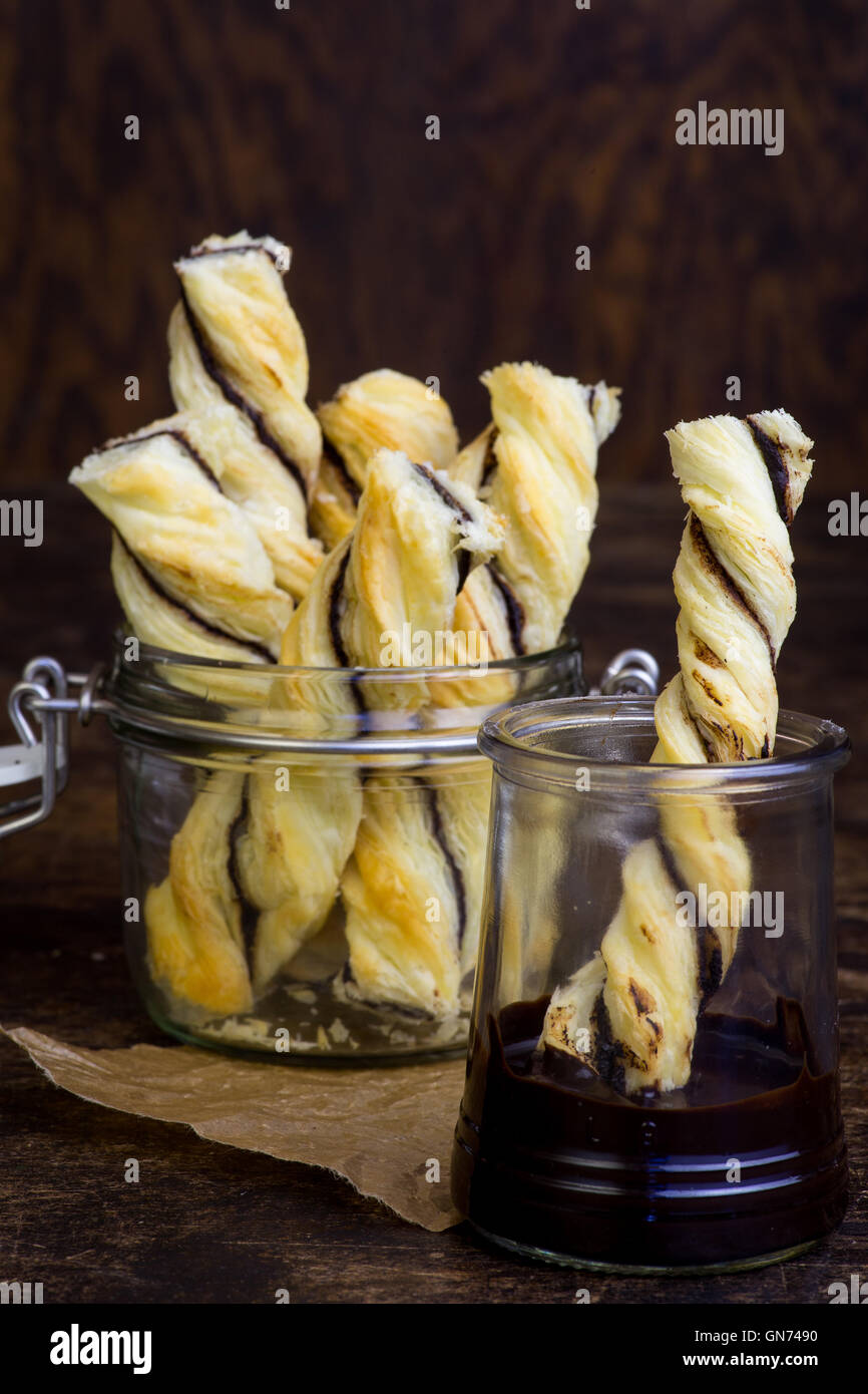 Homemade danish puff pastry twists dipped into melted chocolate in small jar on dark background Stock Photo