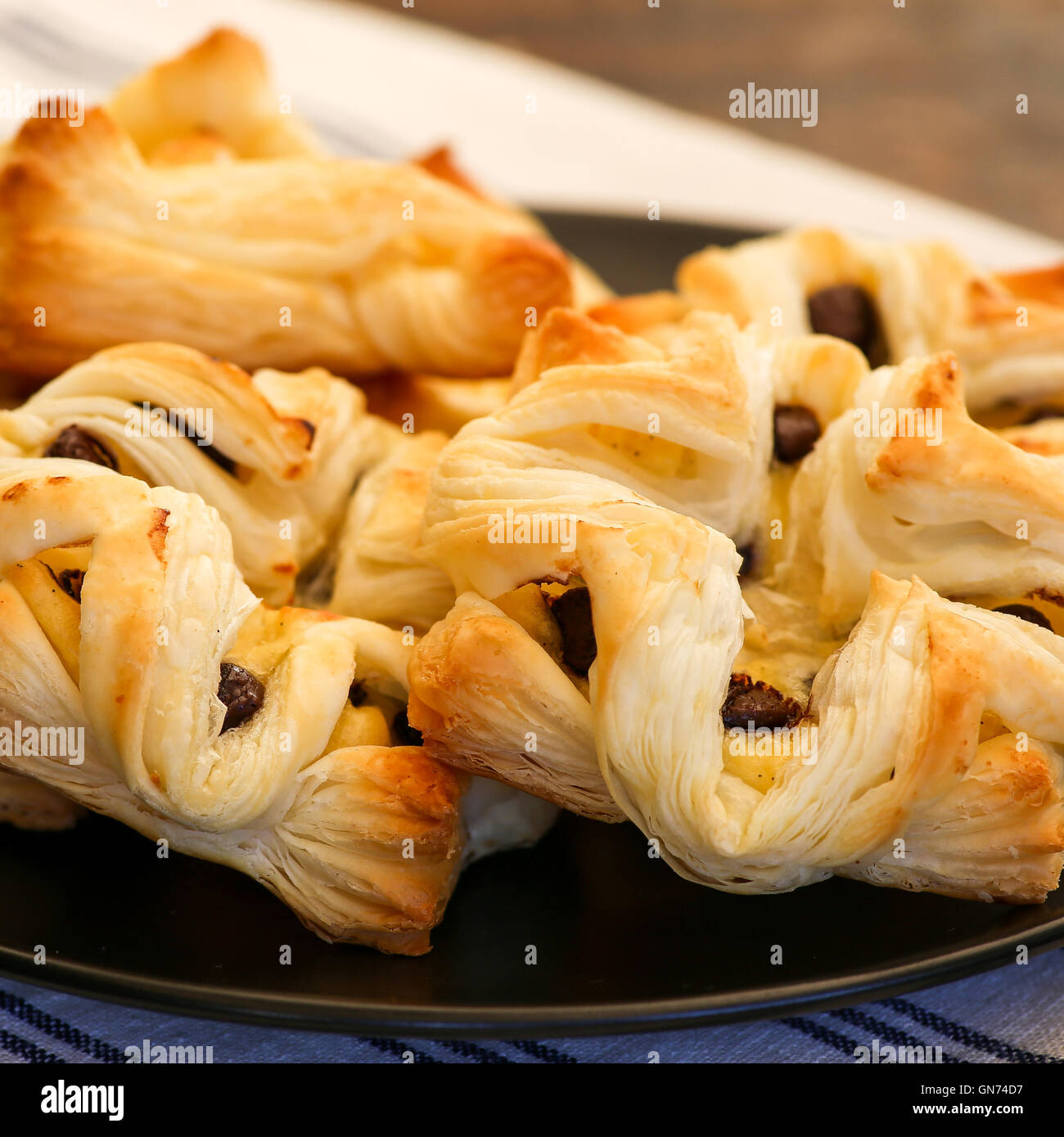 Danish puff pastry flowers and diamonds with vanilla pastry cream and chocolate chips drops on black plate Stock Photo