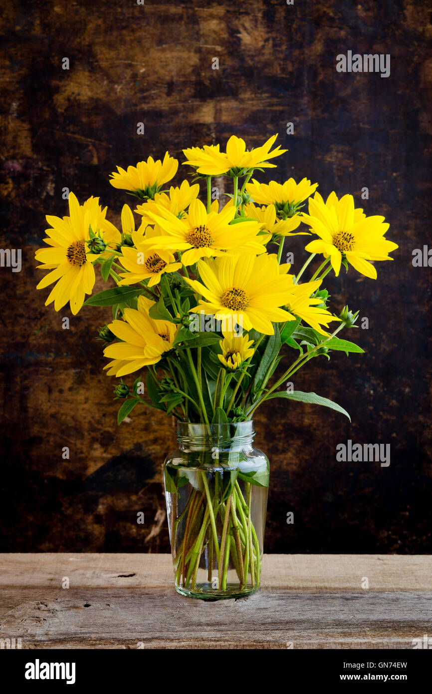Still life with rudbeckia bright yellow flowers bouquet in glass jar on dark rustic background Stock Photo