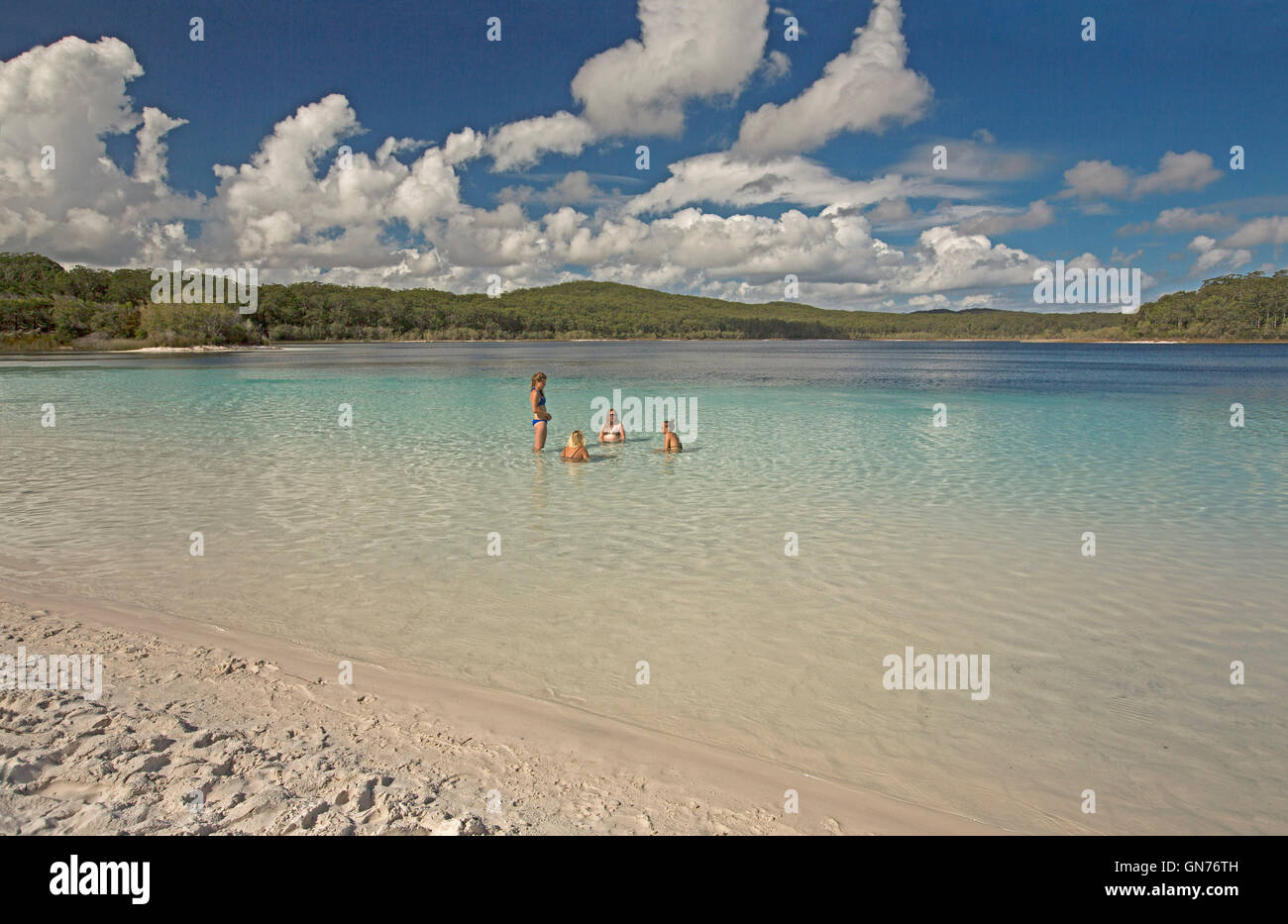 Lake Mackenzie with group of tourists in turquoise water over white sand hemmed by forests & under blue sky on Fraser Island Stock Photo