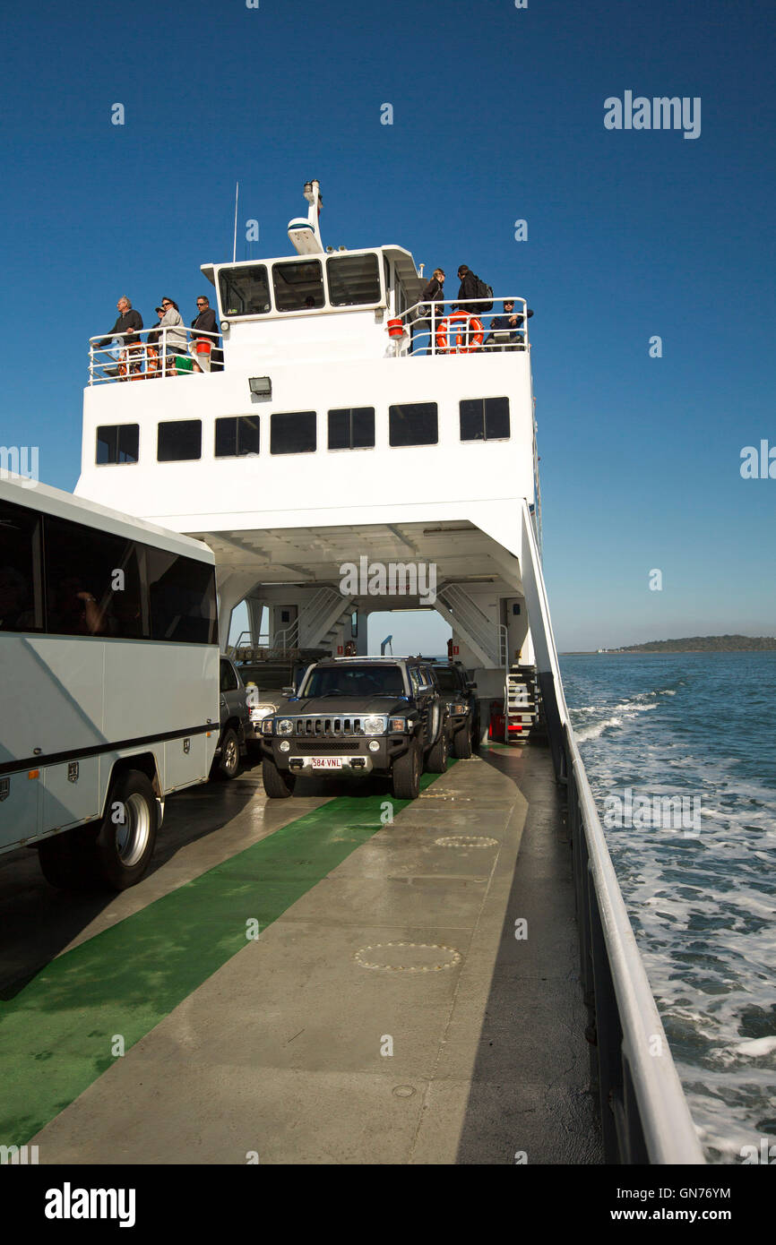 Vehicles parked on ferry with passengers standing on upper deck on voyage across blue ocean waters to Fraser Island Australia Stock Photo
