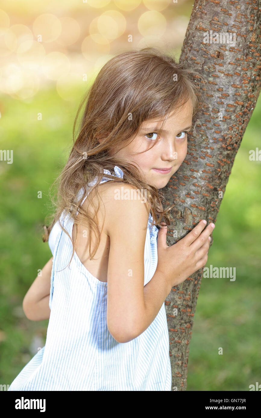 Smiling little girl hugging a tree in the park Stock Photo - Alamy