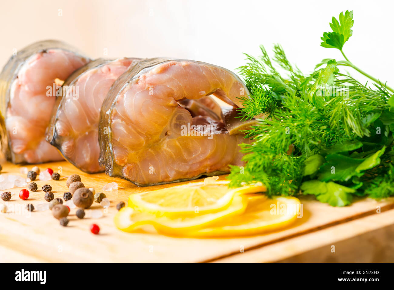 fresh raw sturgeon sliced fish with greens, lemon, different peppers and salt on wooden background, closeup Stock Photo