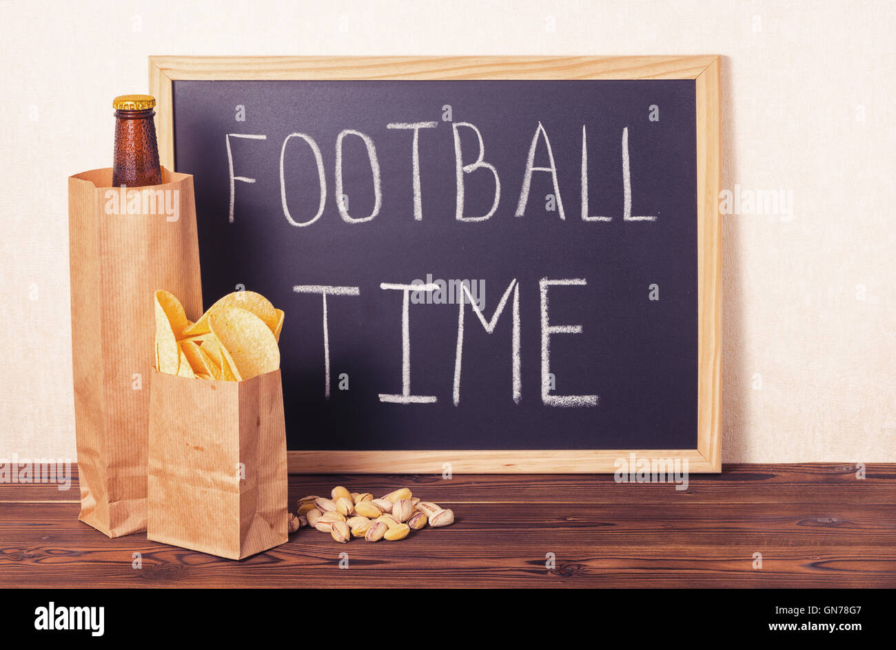 football fans concept of beer bottle in brown paper bag,  chips, pistachio and handwriting text football time written in chalkbo Stock Photo