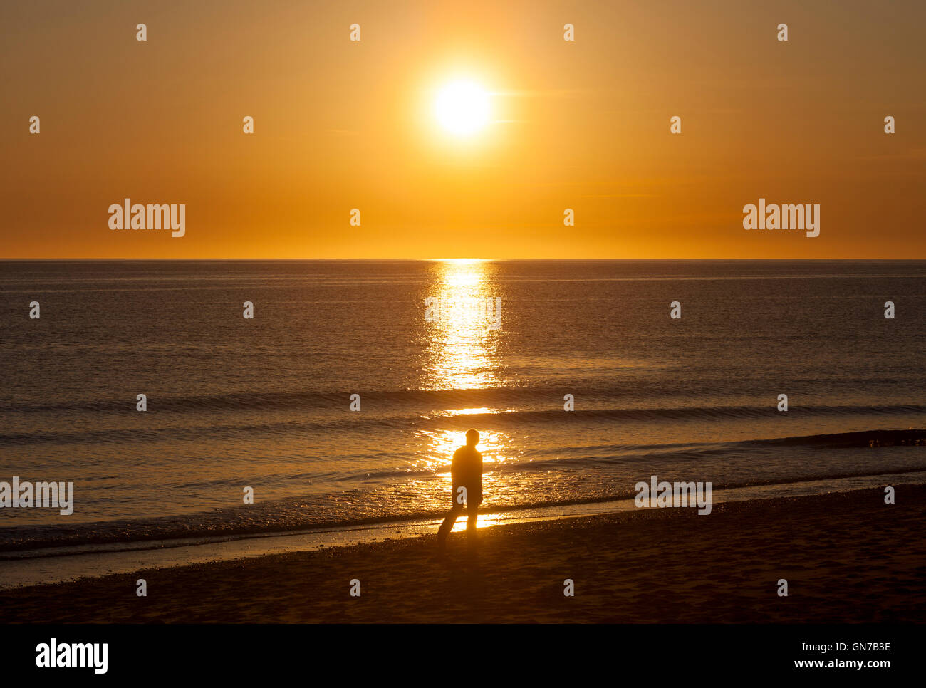 A sunset on the ocean and a silhouette of a person walking on the beach ...