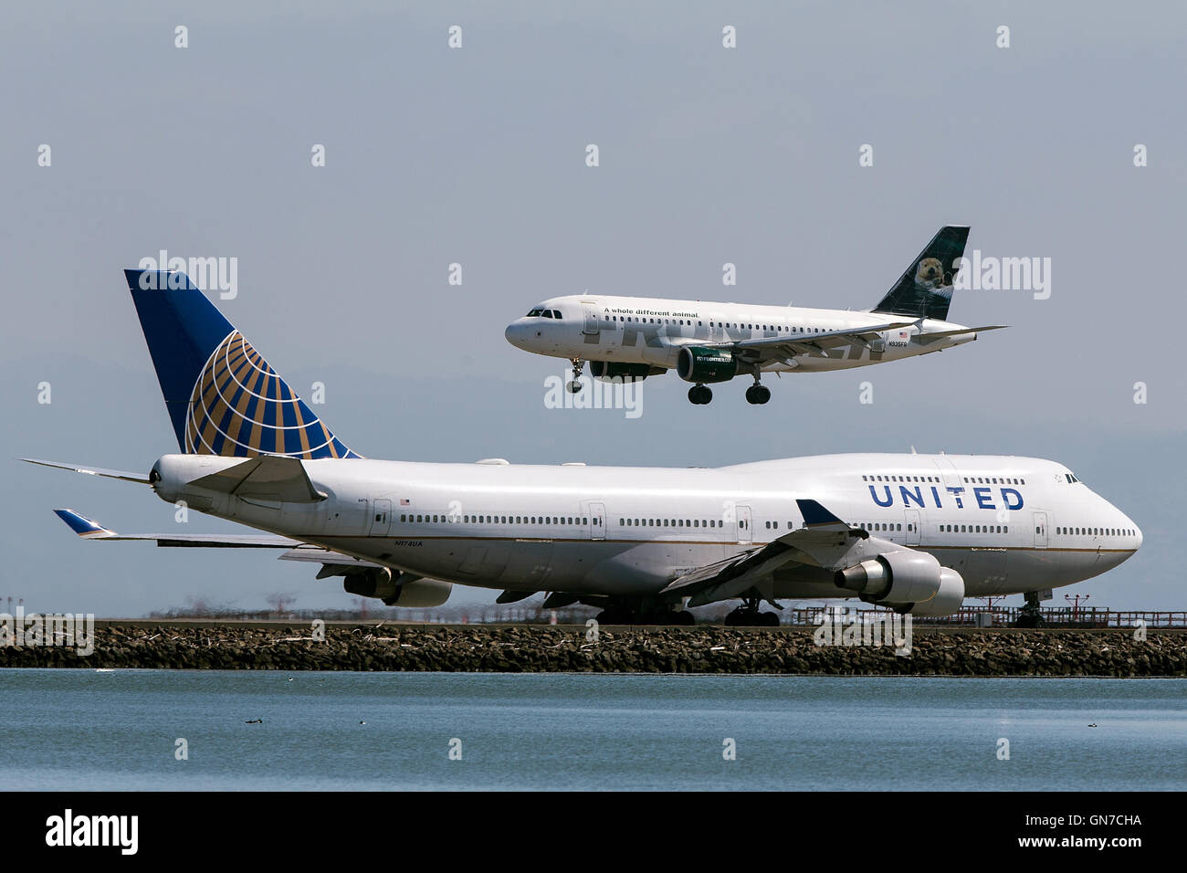 Frontier Airlines Airbus A319-111 (N935FR) lands past United Airlines Boeing 747-422 (N174UA) at San Francisco International Airport (SFO), Millbrae, California, United States of America Stock Photo
