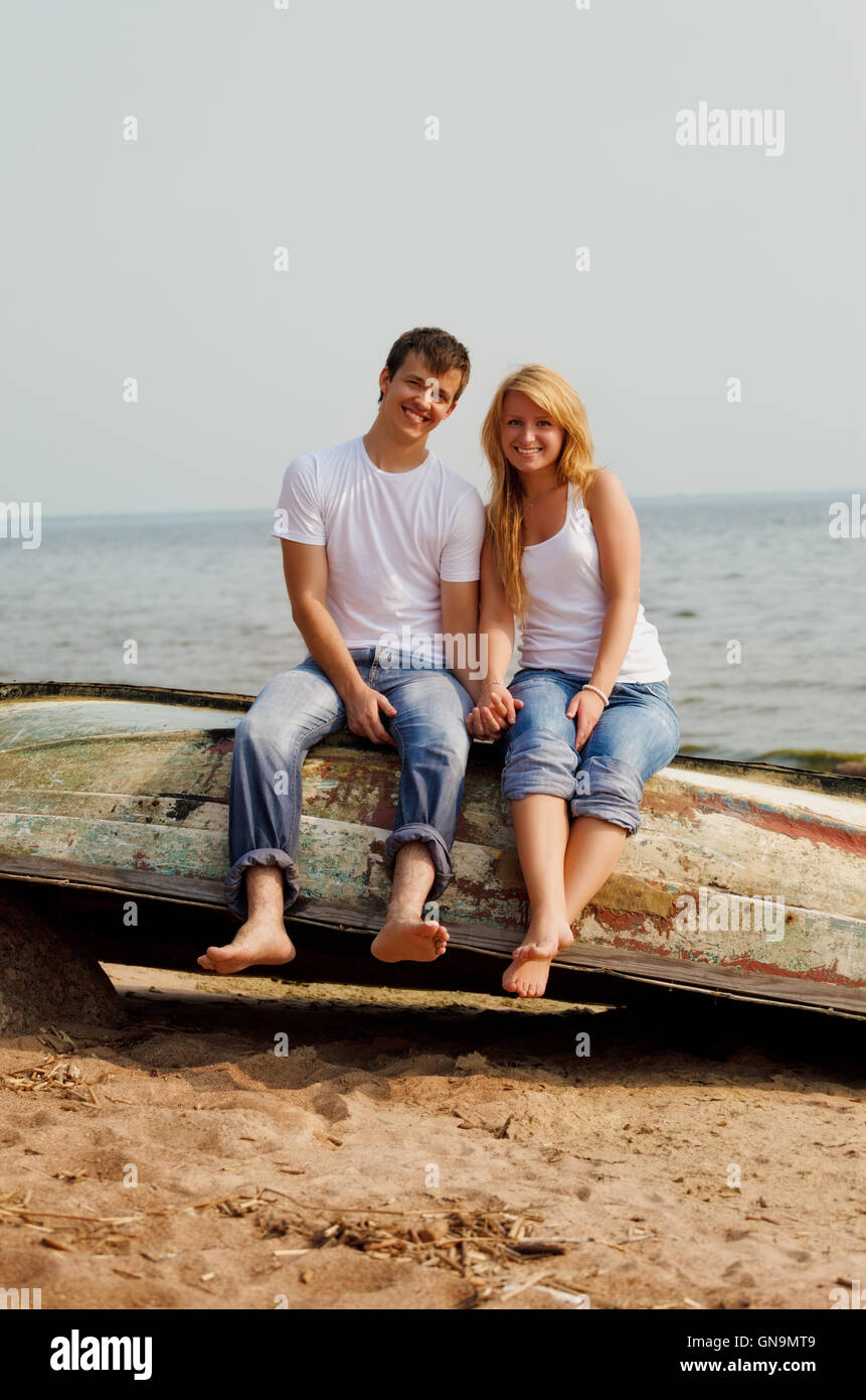 couple on a beach sitting on old boat Stock Photo - Alamy