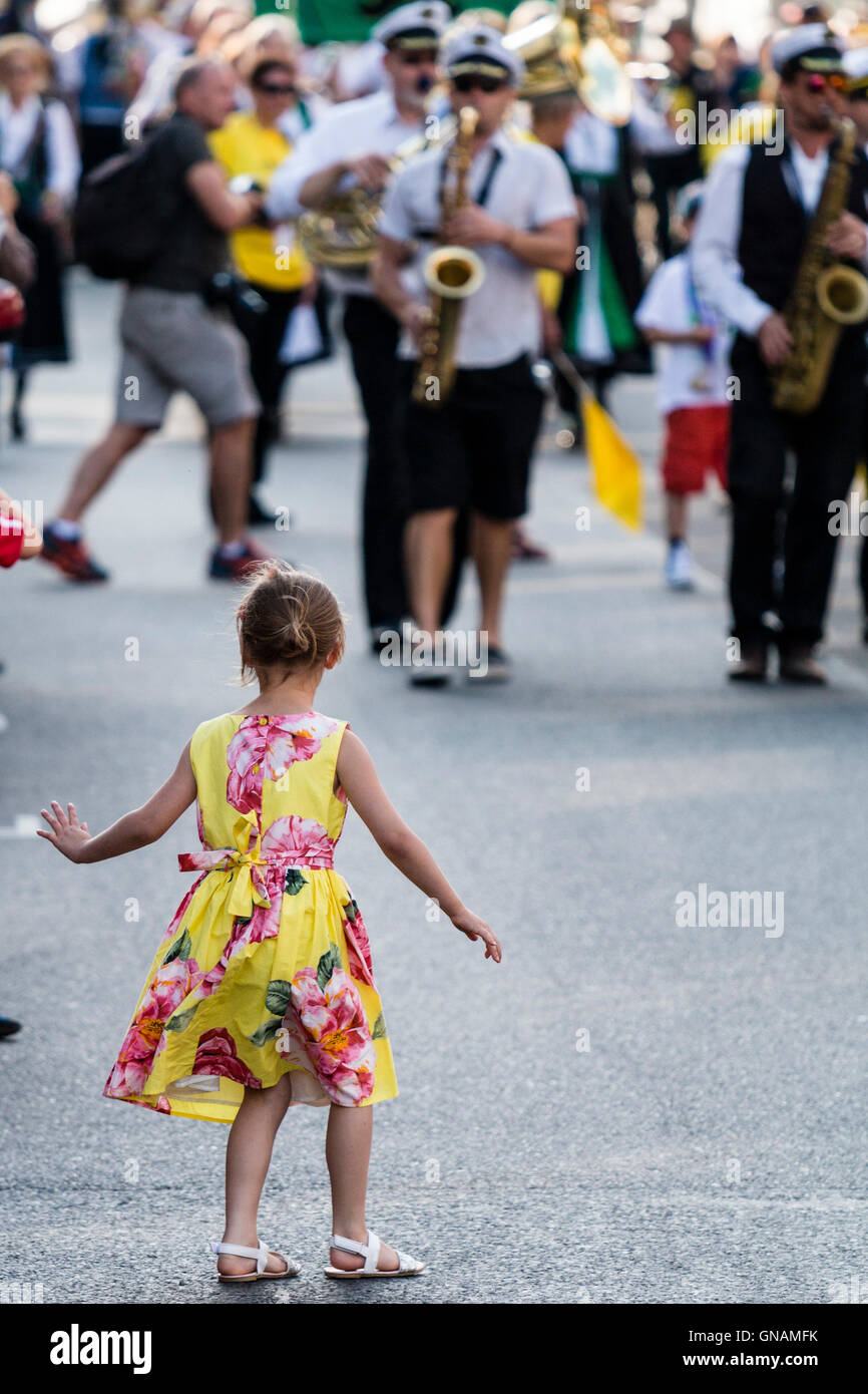 Little girl, 5-6 years old, from audience, stepping out in front of parade and dancing, stealing the show. Parade in background coming towards child. Stock Photo