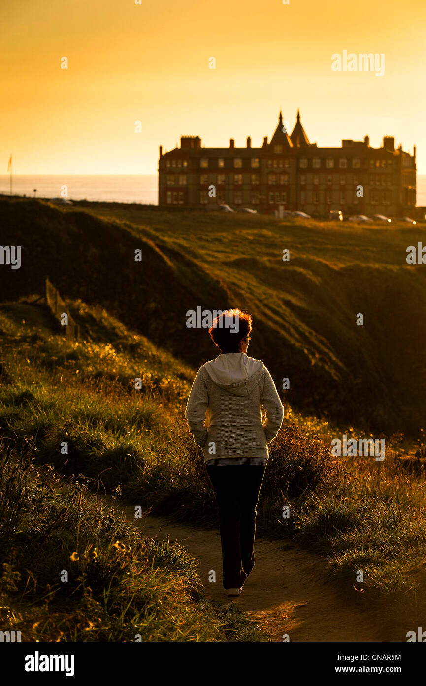 A woman walks along a path during an intense sunset over The Headland in Newquay, Cornwall. Stock Photo