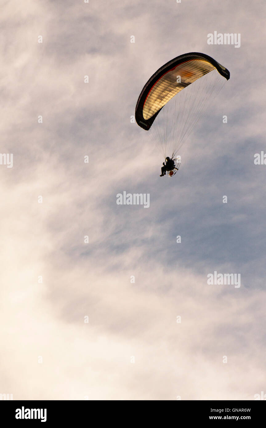 A motorised pararglider flies overhead. Stock Photo
