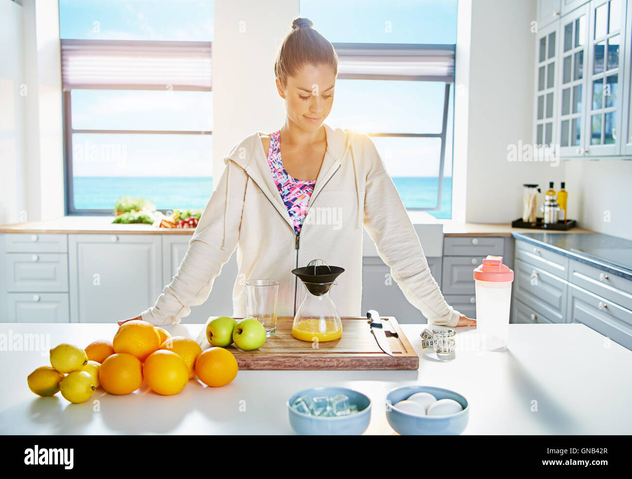Pretty healthy young woman making juice in her kitchen form an assortment of fresh fruit in a healthy diet concept Stock Photo