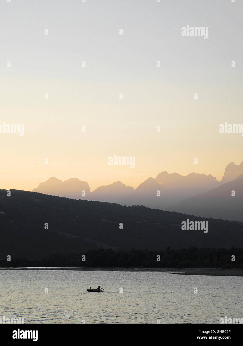 Full frame shot of sunset landscape with mountain, lake, forest and a small fishing boat Stock Photo