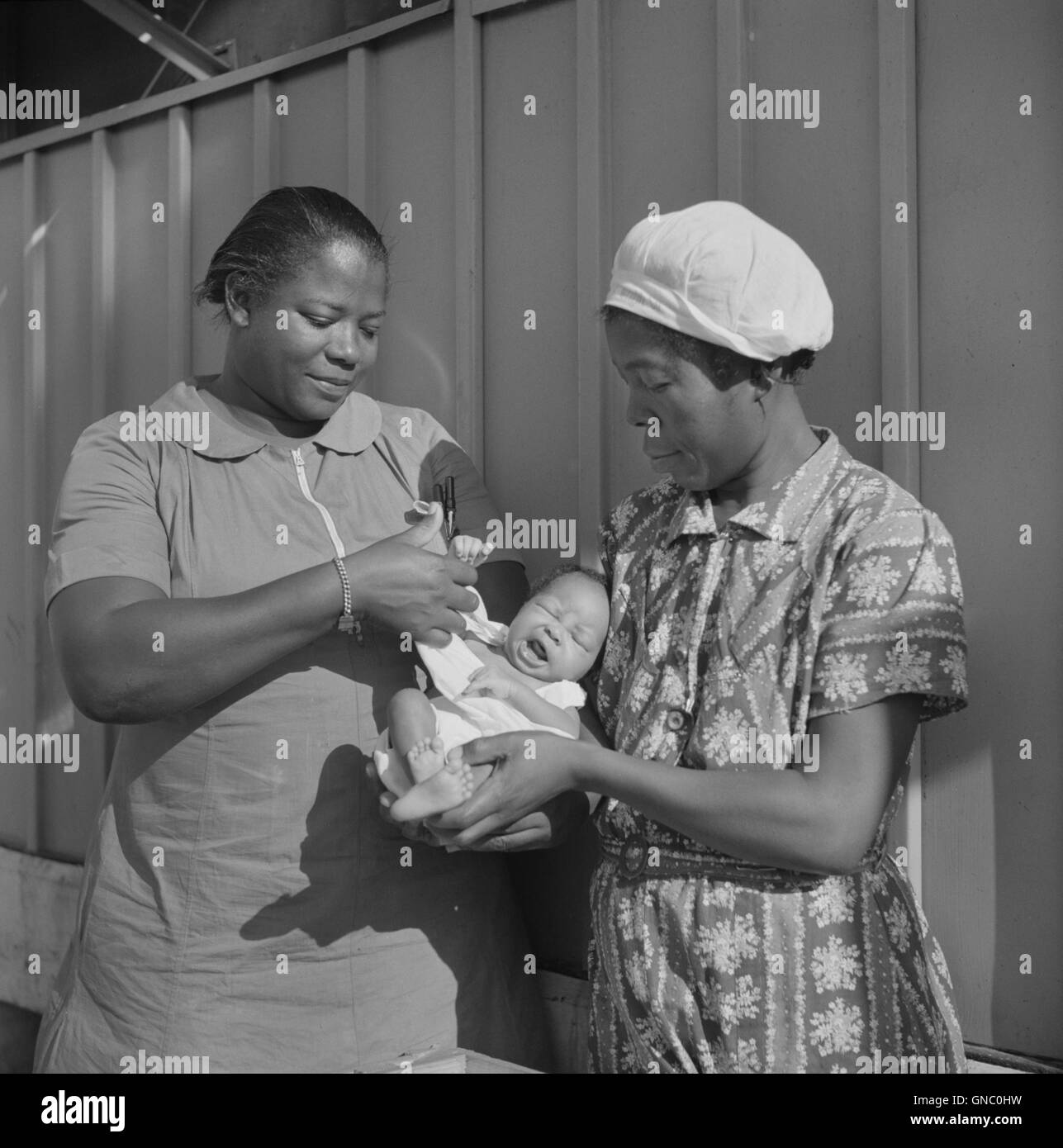 Nurse Examining Infant with Mother and Child Receiving Prenatal and Postnatal Care, Okeechobee Migratory Labor Camp, Belle Glade, Florida, USA, Marion Post Wolcott for Farm Security Administration, June 1940 Stock Photo