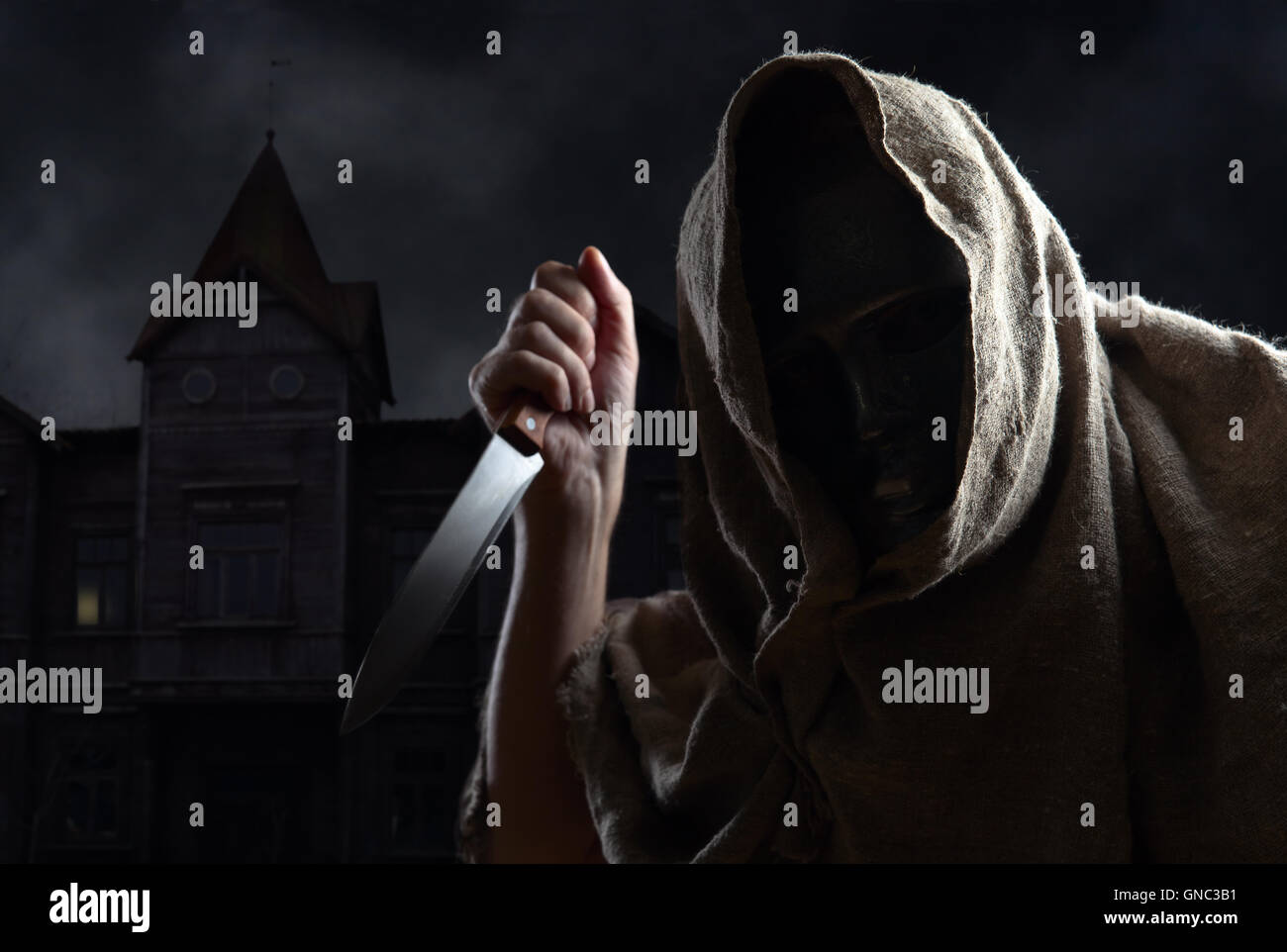 The hooded man in mask with a big knife Stock Photo