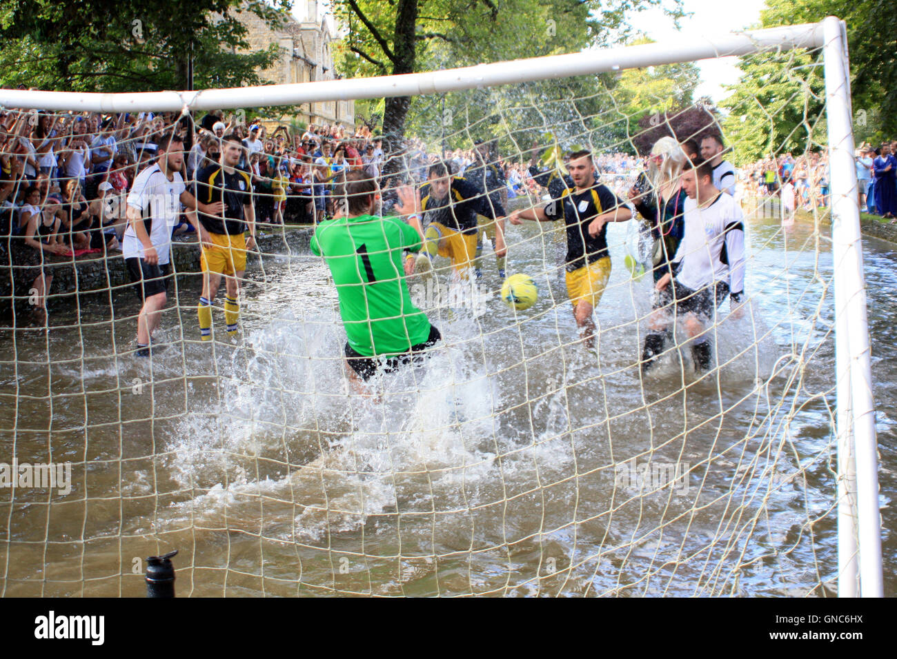 Members of Bourton Rovers 1st XI (dark blue shirts) and the club's 2nd XI (white shirts) battle for the ball during the annual Football In The River match in Bourton-on-the-Water, Gloucestershire. Stock Photo