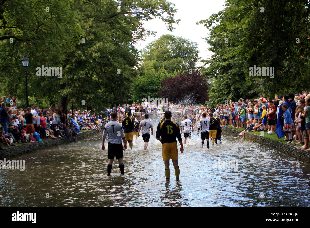 Members of Bourton Rovers 1st XI (dark blue shirts) and the club's 2nd XI (white shirts) battle for the ball during the annual Football In The River match in Bourton-on-the-Water, Gloucestershire. Stock Photo