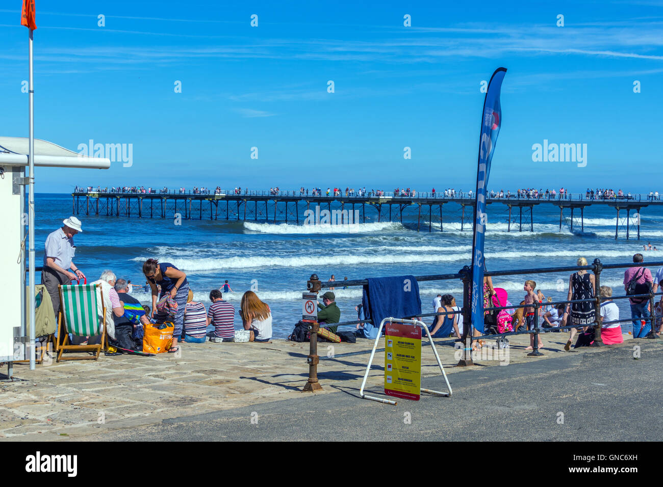People sat on shore with Saltburn by the Sea pier in the background Stock Photo