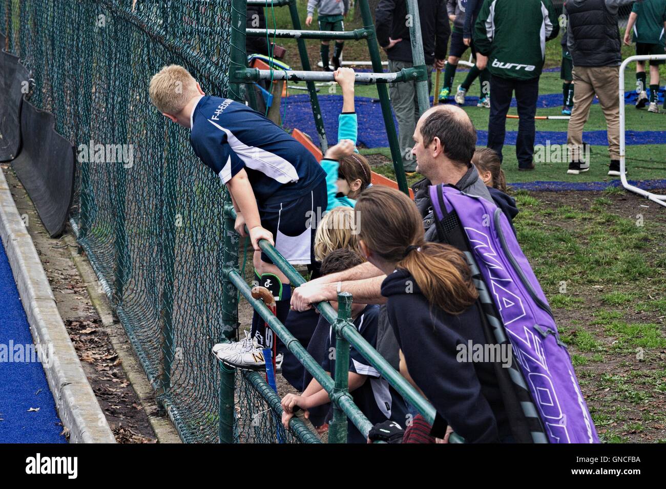 Junior field hockey players watching a hockey game from behind a fence, with their coach. Stock Photo