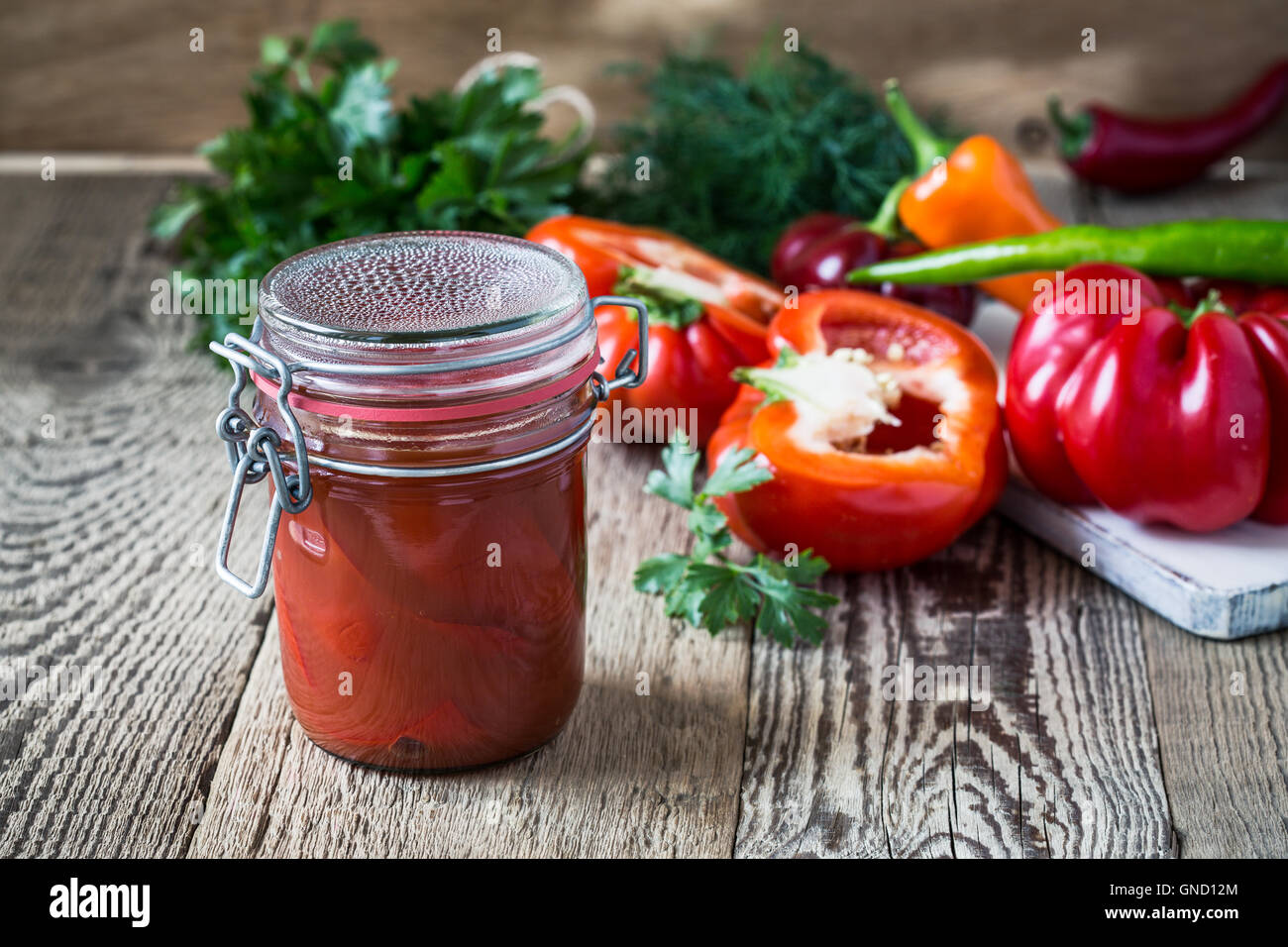 Homemade pickled peppers in tomato juice and sweet bell red pepper on rustic table Stock Photo