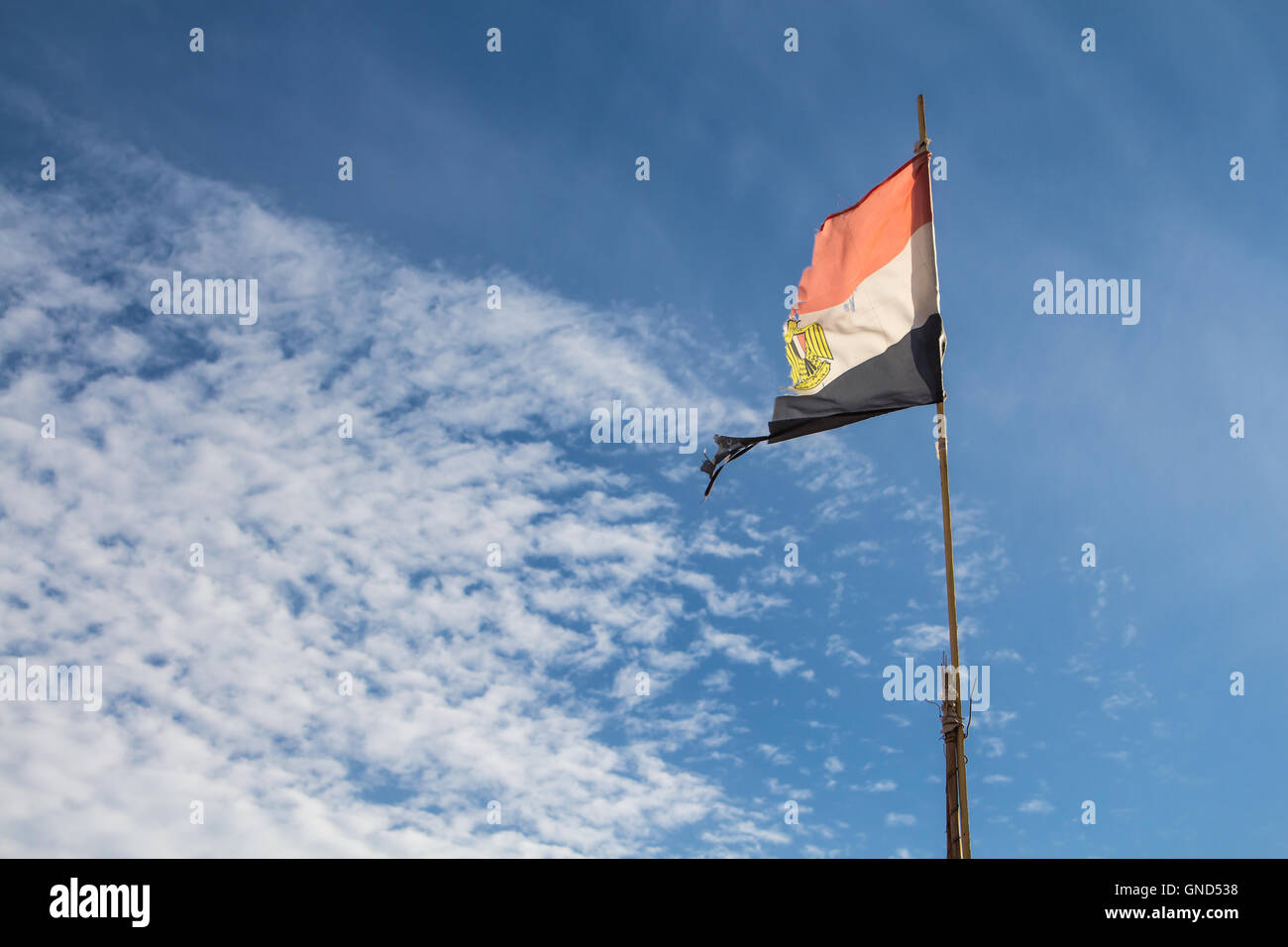 Ragged egyptian flag in the wind, enlightened by sunlight. Blue sky with intense white clouds on the left side. Stock Photo