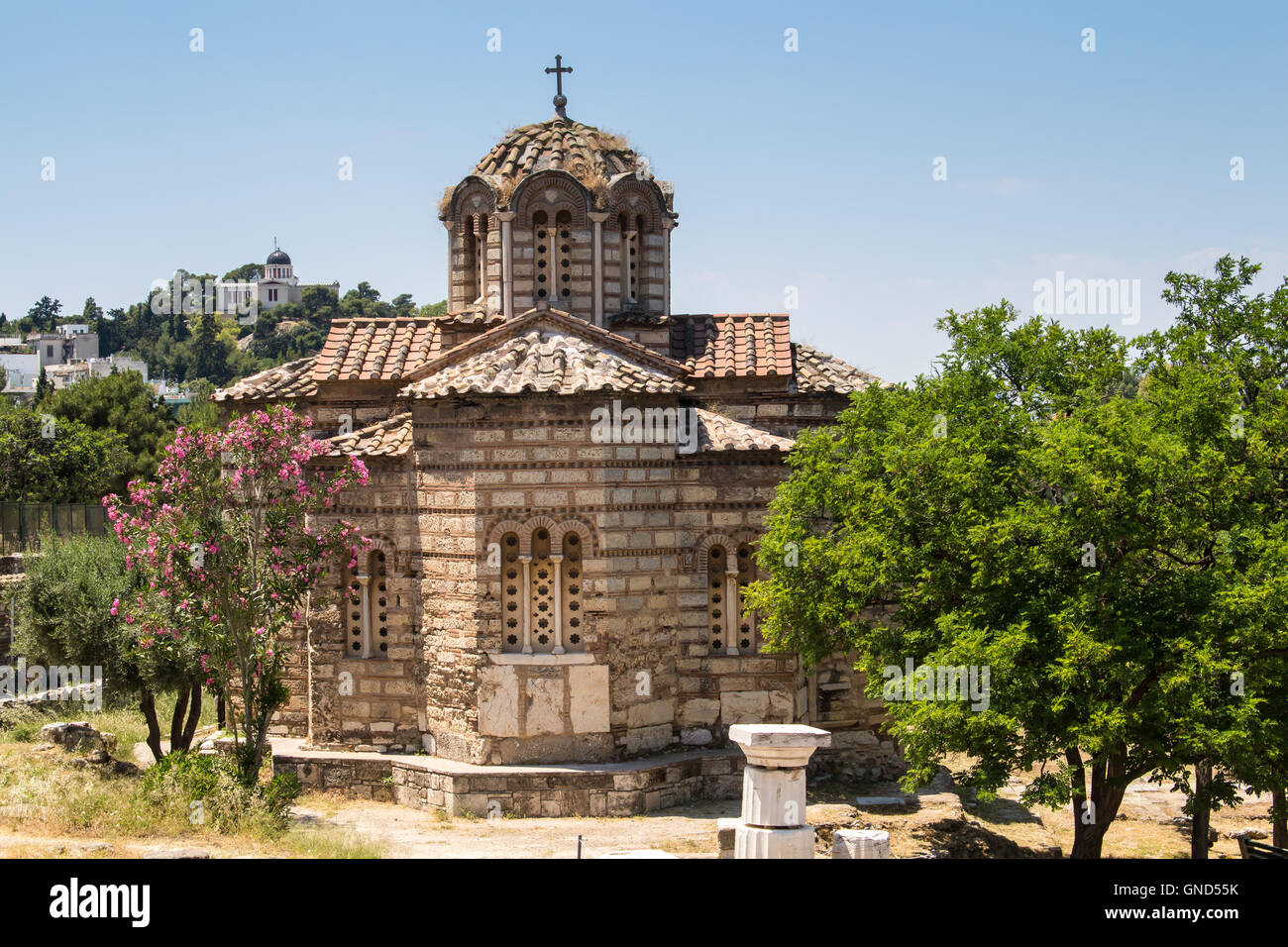 Old orthodox basilica in the city center of Athens. Park with olive and oleander trees. Hill in the background. Blue sky. Stock Photo
