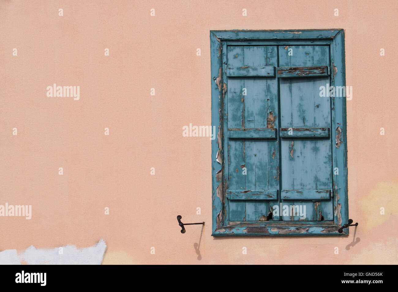 Enlightened light orange wall of a house with a window with an old wooden blue closed shutter. Plaka district of Athens, Greece. Stock Photo