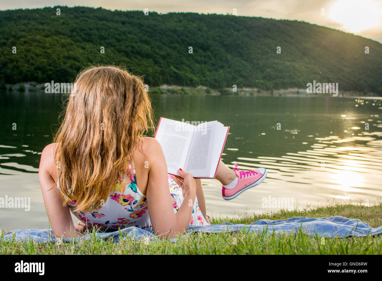 Girl reading a book by the lake. Summertime leisure Stock Photo