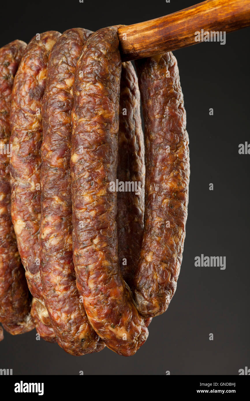 hanging smoked traditional sausage on a stick on black background Stock